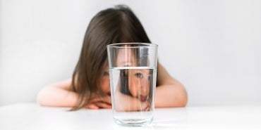 Girl behind water glass | One Water Issues: The Nexus of Drinking Water Supply Management, Lead and Copper Rule Compliance, and Recycled Water