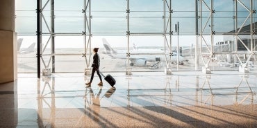 traveler with suitcase walking through airport terminal with sun coming through windows