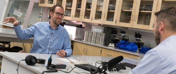 Photo of a man speaking with enthusiasm in front of a mic