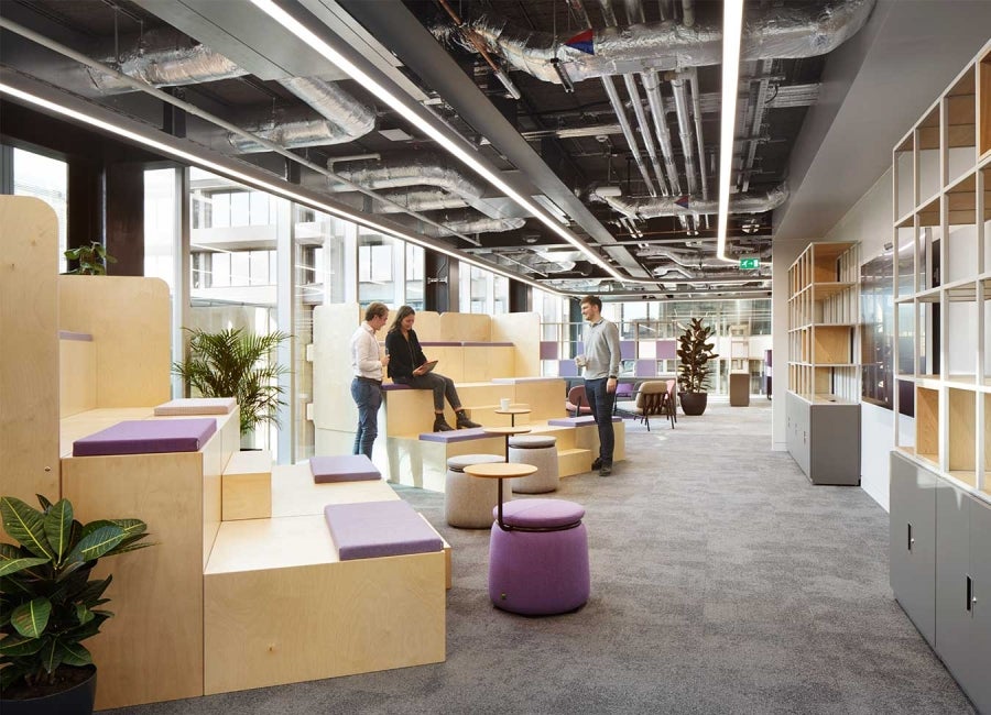 Open-plan office at One Braham, London, UK. Wooden benching in foreground.