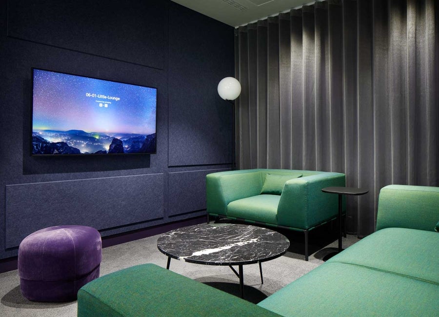 Workspace at One Braham, London, UK. Display screen fixed to wall with green sofas.