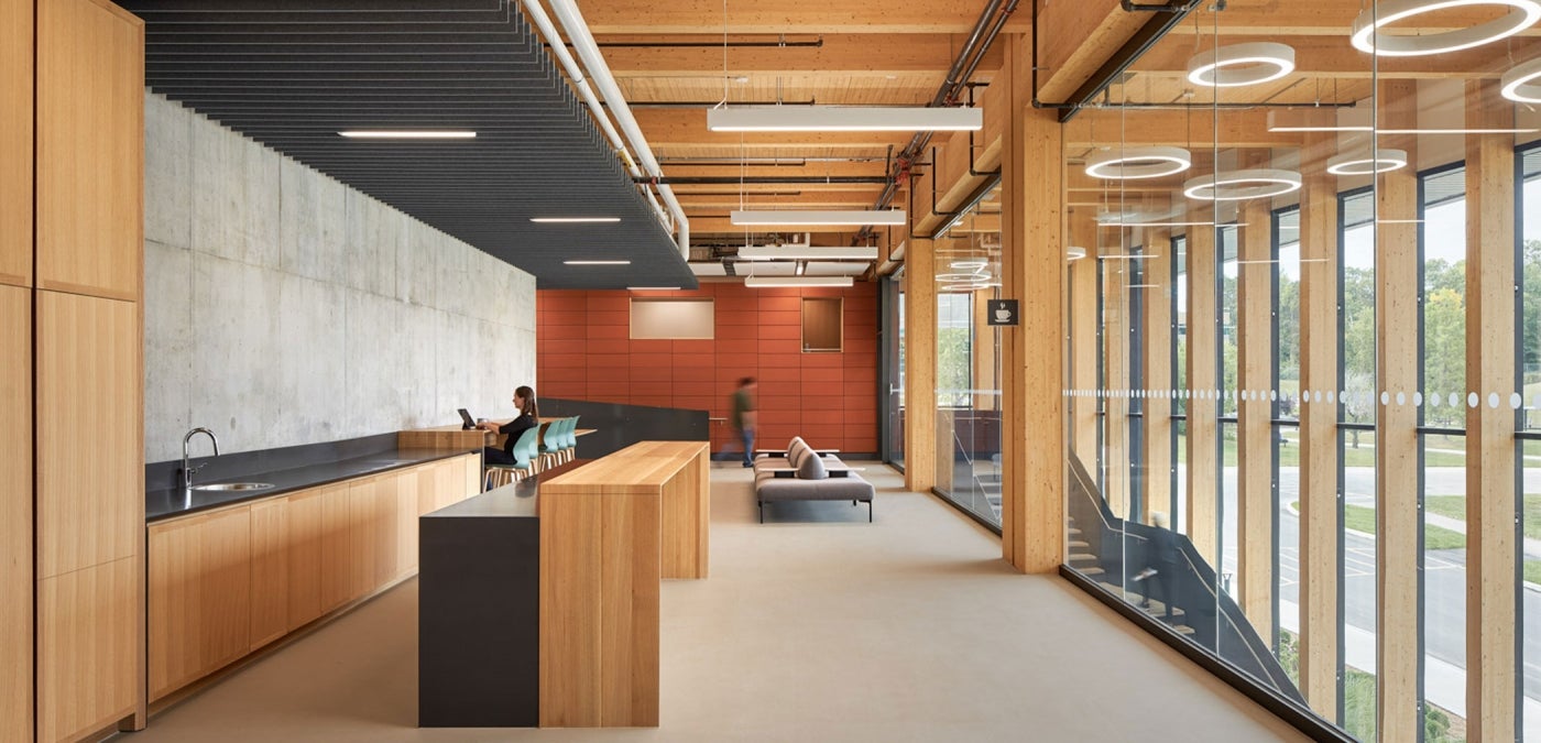 Second floor of a building with mass timber interiors and halo light fixtures. Floor-to-ceiling windows bring natural light in