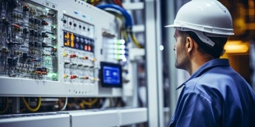 Electrical Engineer in a safety hatn looking at a switchboard.