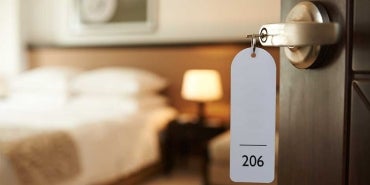 Open hotel room door with handle in foreground and hotel bed in the background.