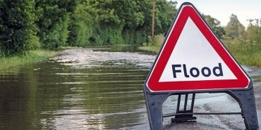 Flood caution sign placed ahead of flood waters over a roadway.