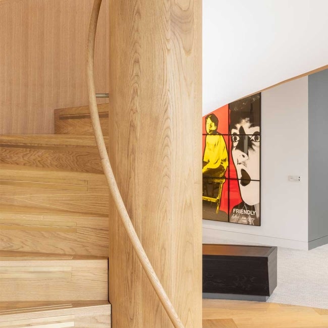 Bottom of wooden spiral staircase with artwork displaying in the background.