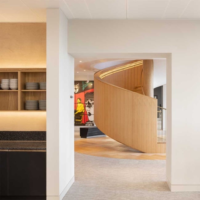 Kitchen unit, with shelves of bowls and plates stacked. Wooden spiral staircase in the background and artwork on the wall.