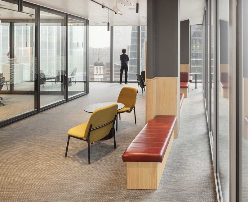 Workspace interior at 22 Bishopsgate, London. Chairs and benches are within frame. A man is stood by the window, looking out at the London scenery.