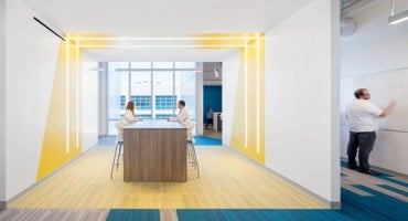 Students sitting at a table wearing lab coats in an open space with yellow accents on the wall