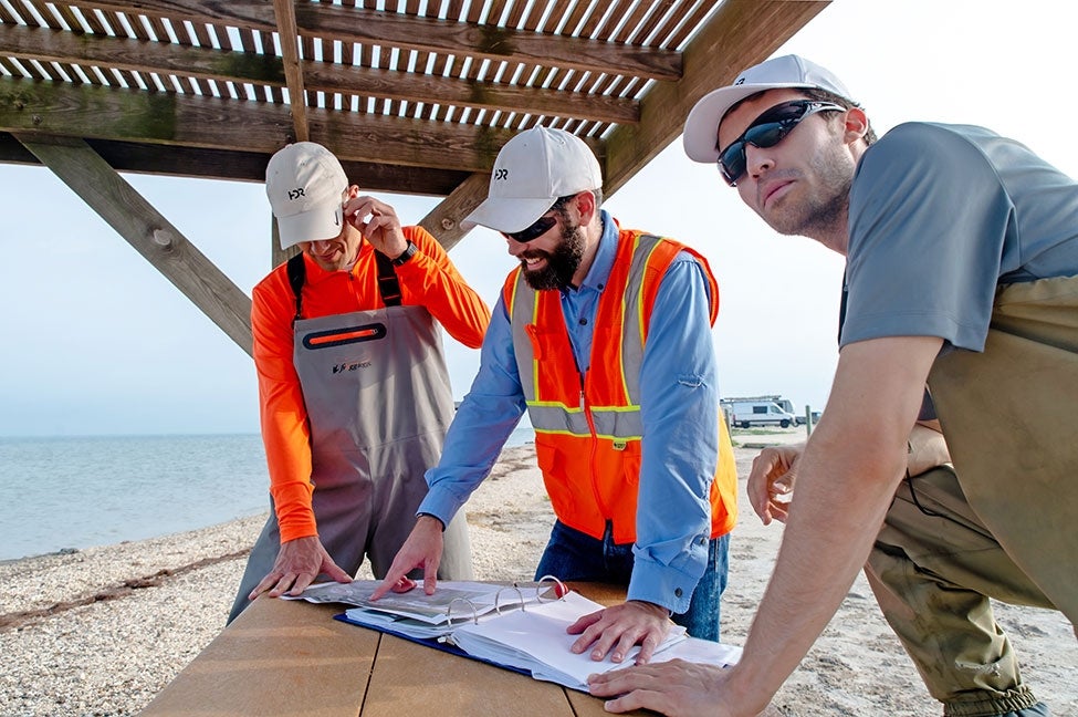 three men collaborate on plans at a picnic table