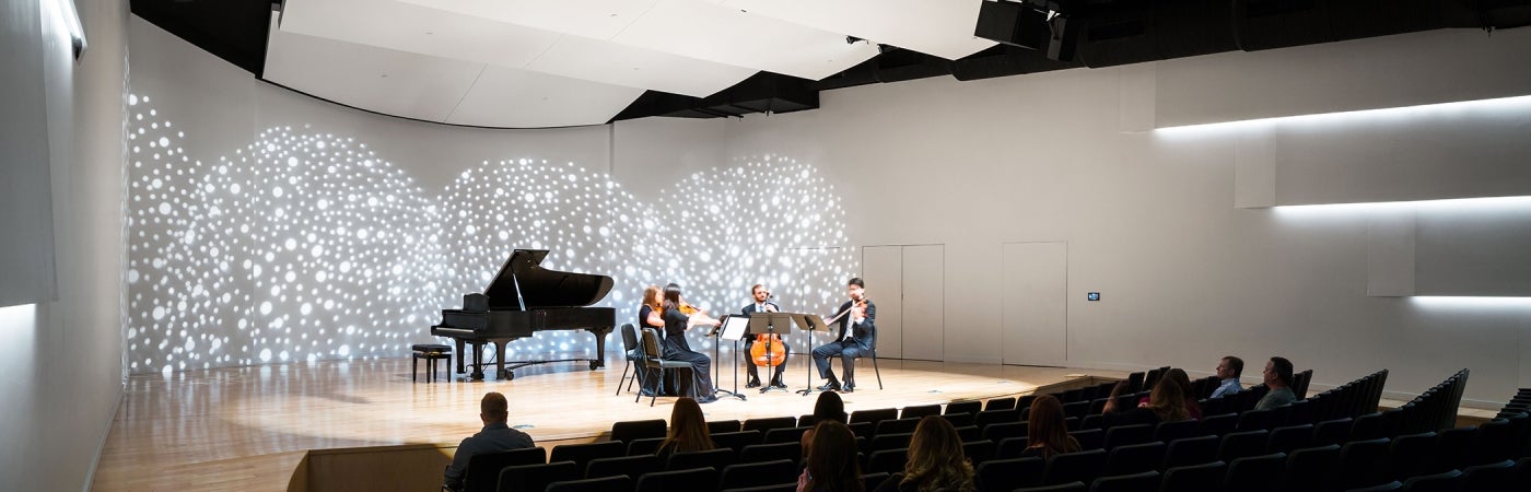 professional architectural photograph of an interior auditorium for musical performances with a piano and classical instruments being played on stage to a small audience in the seats