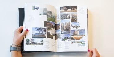 overhead view of open book spread with project photography, a set of hands holds the pages open