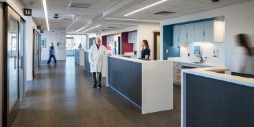 Interior shot of hospital corridor with reception areas. There are medical professionals walking throughout the shot.