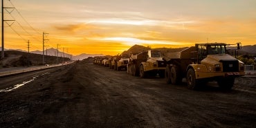 construction vehicles on highway with sun setting behind