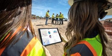 people on construction site looking at tablet with dashboard information