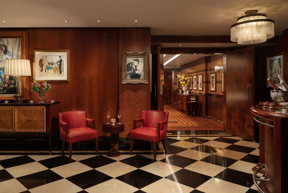 Hotel lobby interior of The Beaumont Hotel, with a chequered marble floor, framed pictures on the wall and furniture.