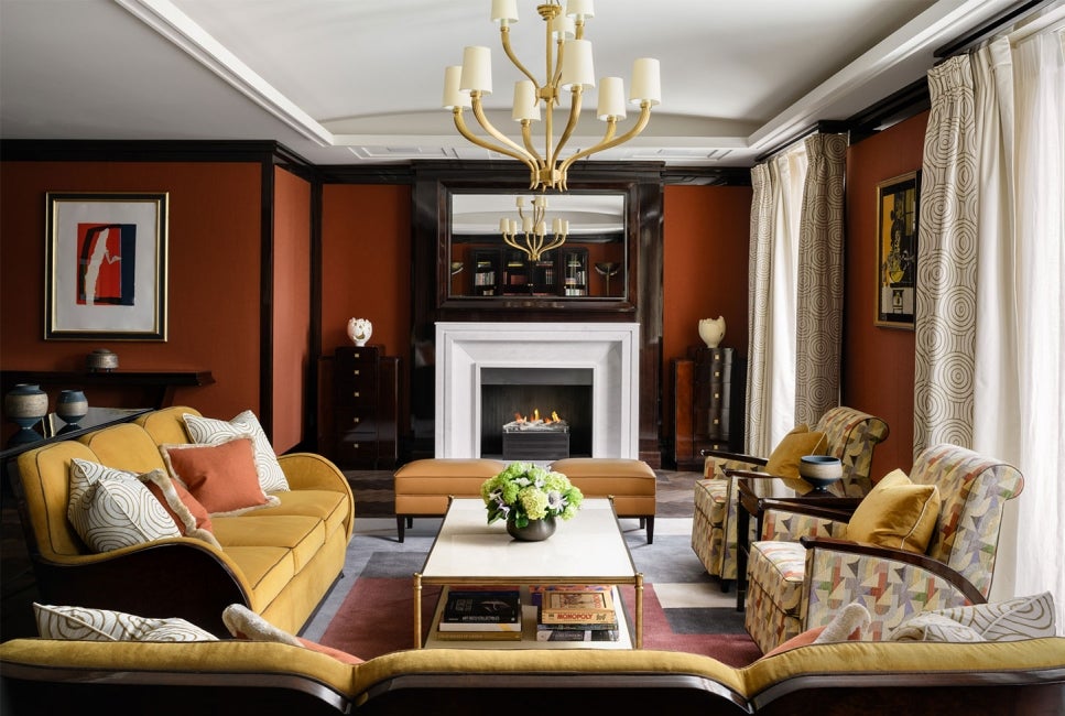 Lounge area at The Beaumont Hotel, with a coffee table surrpunded by furntiture, a fireplace in the background and a chandelier hanging from the ceiling. 