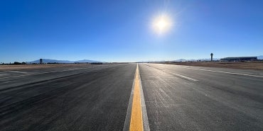 paved airport taxiway with sun in sky