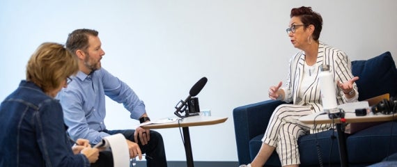 Three people having a discussion around a table with a mic in the center.